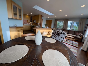A modern kitchen with a dining area, a sofa, and a large window.