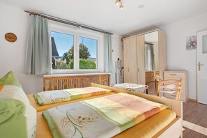 Une chambre avec deux lits, une armoire en bois, un bureau et une fenêtre avec des rideaux.