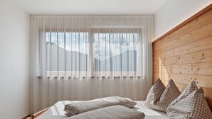 A bedroom with a bed, checkered pillows, sheer curtains, and a wooden headboard. - Apartment '1' with Mountain View, Shared Terrace and Wi-Fi (Bolzano)
