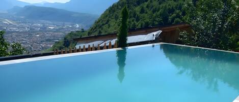 A clear blue infinity pool with a view of a cityscape and mountains in the background.