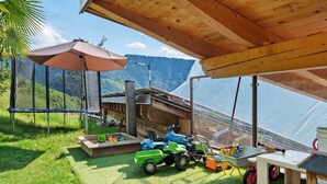 A covered outdoor area with a wooden ceiling, a play area with toy vehicles, and a view of a mountainous landscape. - Apartment 'Lärche' with Mountain View, Shared Terrace and Wi-Fi (Bolzano)