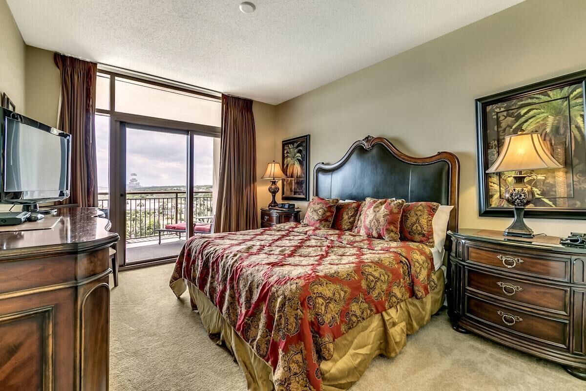 Un dormitorio amplio con una cama grande, un aparador, un televisor y un balcón con vistas.