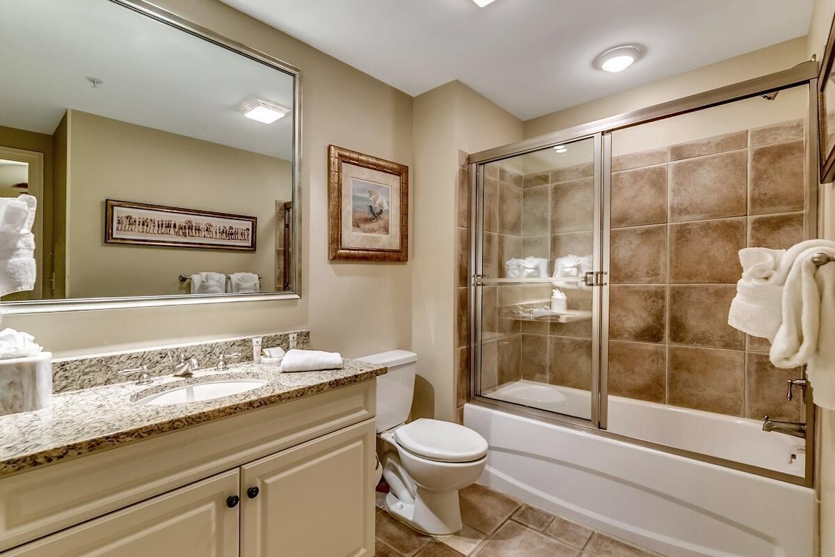 A bathroom with a marble sink, a toilet, a glass-enclosed shower, and a large mirror.