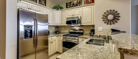 Una cocina con armarios blancos, electrodomésticos de acero inoxidable, encimeras de granito y un elemento decorativo en la pared.