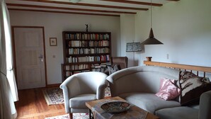 Ein Wohnzimmer mit einer Couch, zwei Sesseln, einem Couchtisch, einem Bücherregal und einer Pendelleuchte.