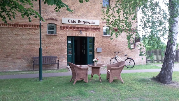 Ein Café namens Café Bugewitz mit roter Backsteinfassade, einer grünen Tür, Korbmöbeln und einem Fahrrad vor der Tür.