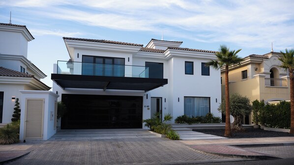 A modern two-story house with a large garage, a covered entryway, and a landscaped front yard with palm trees.