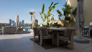 Eine Dachterrasse mit Esstisch, Stühlen und Sonnenschirmen.