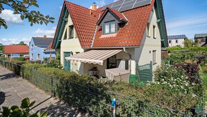 A house with a sloped roof, solar panels, a small balcony, and a garden. - Bungalow 'Manni' with Shared Terrace, Garden, and Wi-Fi (Koserow)