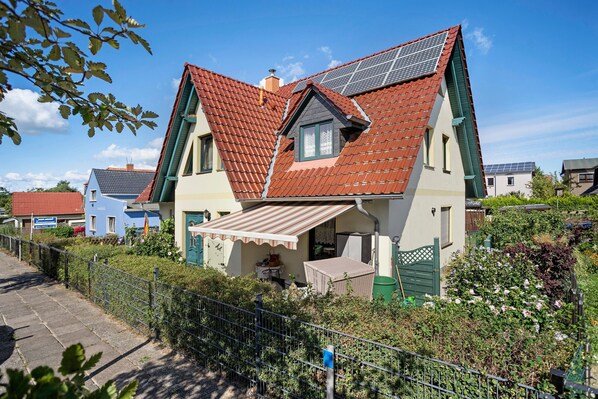 A house with a sloped roof, solar panels, a small balcony, and a garden.