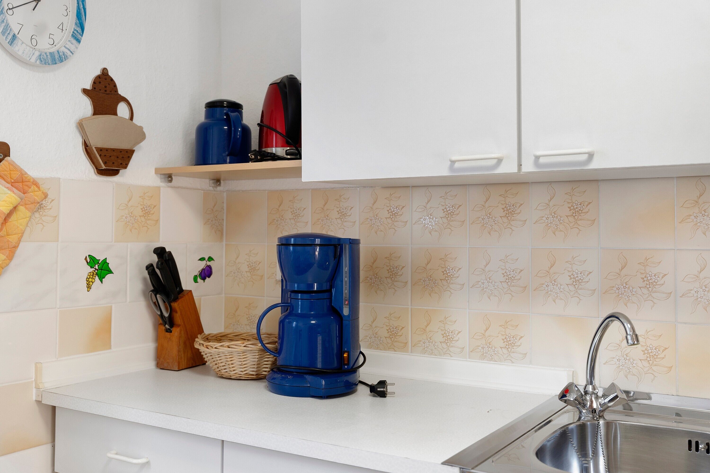 Une cuisine équipée d’une machine à café, d’un évier et d’une horloge murale.