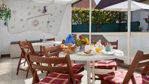 A dining area with a table set for breakfast, chairs, and a decorative wall. - Bungalow 'Manni' with Shared Terrace, Garden, and Wi-Fi (Koserow)
