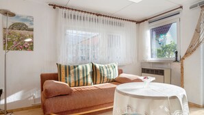 A living room with a sofa, a round table, a floor lamp, and a window with curtains. - Bungalow 'Manni' with Shared Terrace, Garden, and Wi-Fi (Koserow)