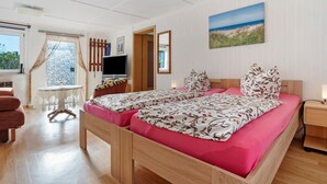 A room with two beds, a TV, a table, and a painting on the wall. - Bungalow 'Manni' with Shared Terrace, Garden, and Wi-Fi (Koserow)