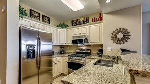 A kitchen with white cabinets, stainless steel appliances, granite countertops, and a decorative wall piece.