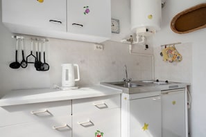 Una cocina con armarios blancos, cafetera, pileta y estufa.