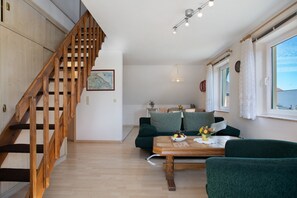 Un escalier menant à une chambre à coucher située en mezzanine, un coin repas avec une table en bois et un canapé vert.