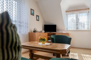 Une pièce comprenant une table à manger, une chaise verte, un téléviseur posé sur un meuble en bois et une fenêtre ornée de rideaux à motifs.