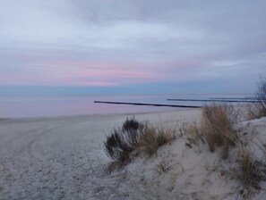 Una playa con dunas de arena y un mar tranquilo bajo un cielo nublado.