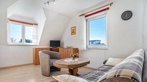 Ein Zimmer mit einer Couch, einem Holztisch, einem Stuhl, einem Fernseher und einer Uhr an der Wand.