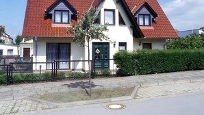 Ein zweigeschossiges Haus mit rotem Ziegeldach, grüner Tür und einem kleinen Baum im Vorgarten.
