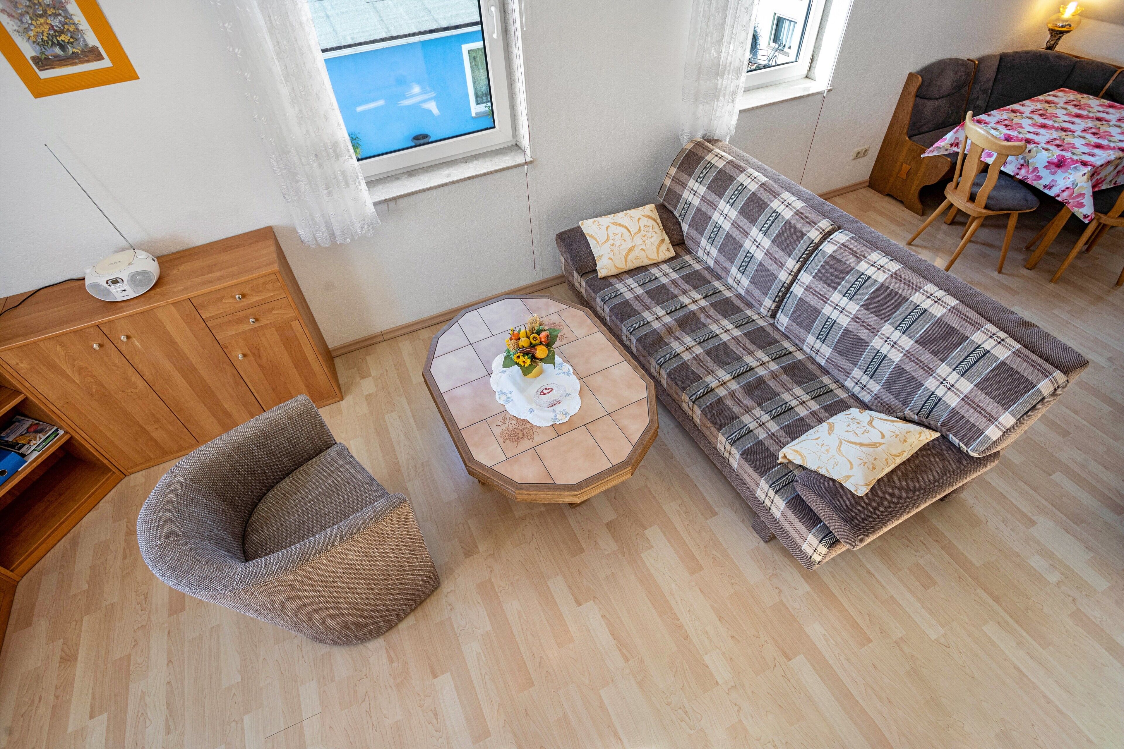 A cozy living room with a sofa, a small round table with a vase, a wooden cabinet, and a window with curtains.