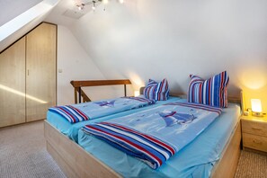 Quarto com teto inclinado, estrutura de cama de madeira, mesa de cabeceira e abajur.
