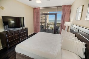 Ein Hotelzimmer mit einem großen Bett, einem Fernseher, einem Schminktisch und einem Balkon mit Meerblick.