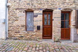 A stone building with a wooden door, a window with a decorative screen, and a number plaque.