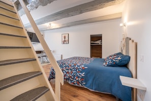 A bedroom with a bed, a wooden headboard, a staircase, and a small desk with a chair.