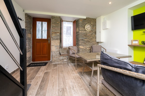 A room with a stone wall, a wooden door, a wicker sofa, a glass table, and a clock on the wall.