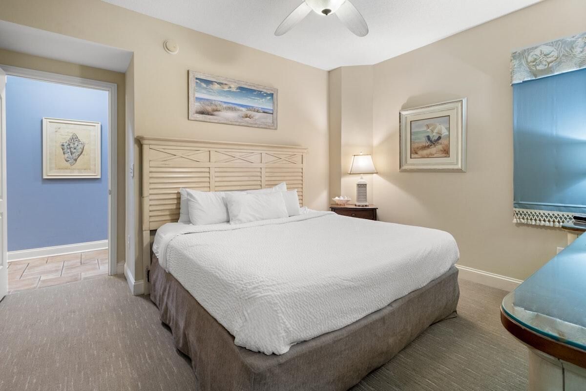 Une chambre d’hôtel avec un grand lit, une table de chevet avec une lampe et deux tableaux encadrés accrochés aux murs.