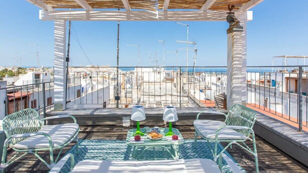 A rooftop terrace with a pergola, two lounge chairs, a small table with a glass top, and a view of the cityscape and sea. - Le Grind - Terrace with a Great View of the Adriatic Sea and the historic center (Ostuni)