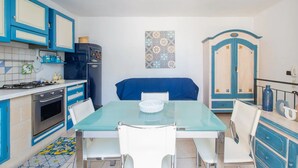 A compact kitchen with blue cabinets, a gas stove, a refrigerator, and a dining table with chairs. - Le Grind - Terrace with a Great View of the Adriatic Sea and the historic center (Ostuni)
