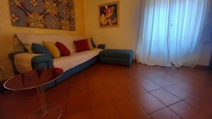A living room with a sofa, a glass coffee table, a painting on the wall, and a window with curtains. - Conti Apartment in Firenze (Florence)