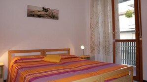 Ein Schlafzimmer mit einem Bett, einem Nachttisch, einer Lampe, einem Fenster mit Vorhängen und einem Gemälde an der Wand.