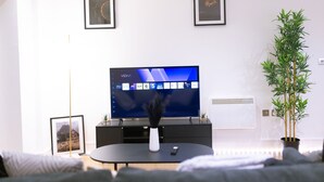 A modern living room with a flat-screen TV, framed pictures on the wall, a potted plant, and a remote control on a coffee table. - Birmingham City Centre Apartment- Sleeps4-freep (Birmingham)