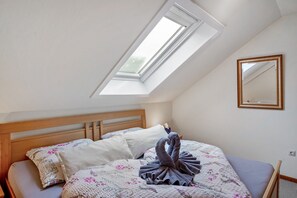 Un dormitorio con tragaluz, una cama con ropa de cama floral, un cabecero de madera y un espejo en la pared.