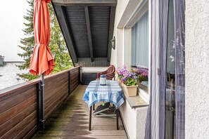 A balcony with a table, chairs, a red umbrella, and potted plants. - Apartment 'Haus Rehblick 2, Apt. 4' with Mountain View, Shared Garden and Wi-Fi (Sankt Andreasberg)