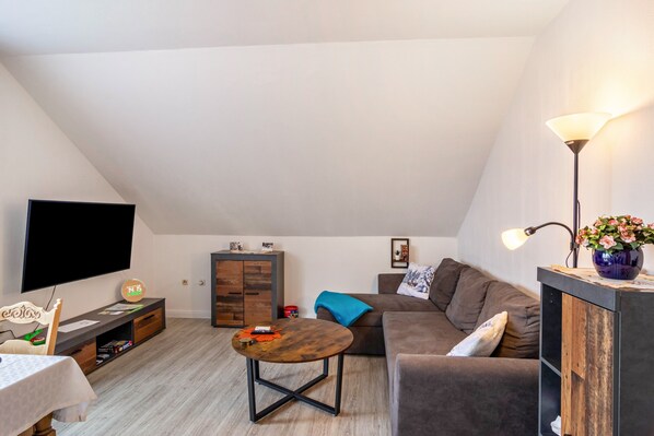 A living room with a flat-screen TV, a wooden coffee table, a sofa, a cabinet, and a lamp. - Apartment 'Haus Rehblick 2, Apt. 4' with Mountain View, Shared Garden and Wi-Fi (Sankt Andreasberg)
