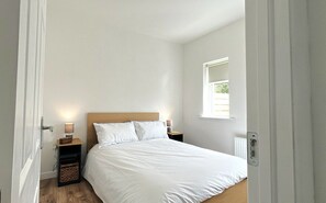 A bedroom with a bed, bedside lamps, a nightstand, and a window. - Culfin Cottage (Renvyle)