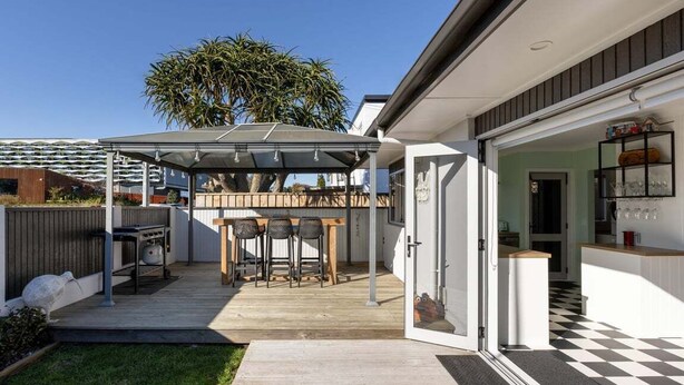 A modern house with a covered patio, a dining area, and a kitchen visible through an open door.