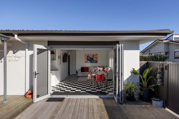 A modern house with a covered patio, a dining area with red chairs, and a checkered floor.