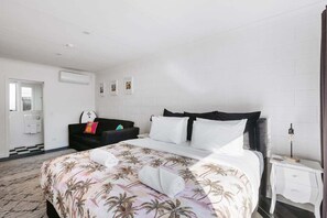 A hotel room with a bed, a black sofa, a nightstand, and a bathroom visible through an open door.