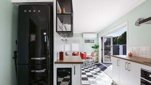 A kitchen with a black Smeg refrigerator, a checkered floor, white cabinets, and a view through a glass door.