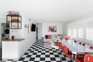 A modern kitchen with a checkered floor, a dining area with red chairs, and a living space with a sofa and artwork.