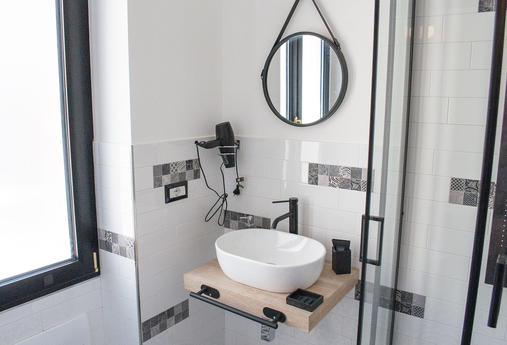 Un bagno con un lavandino bianco, uno specchio rotondo e un asciugacapelli portatile.