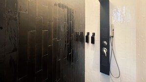 A modern bathroom with black tiled walls, a black showerhead, and a white tiled shower area. - LH 51 Neapolitan Rooms (Naples)