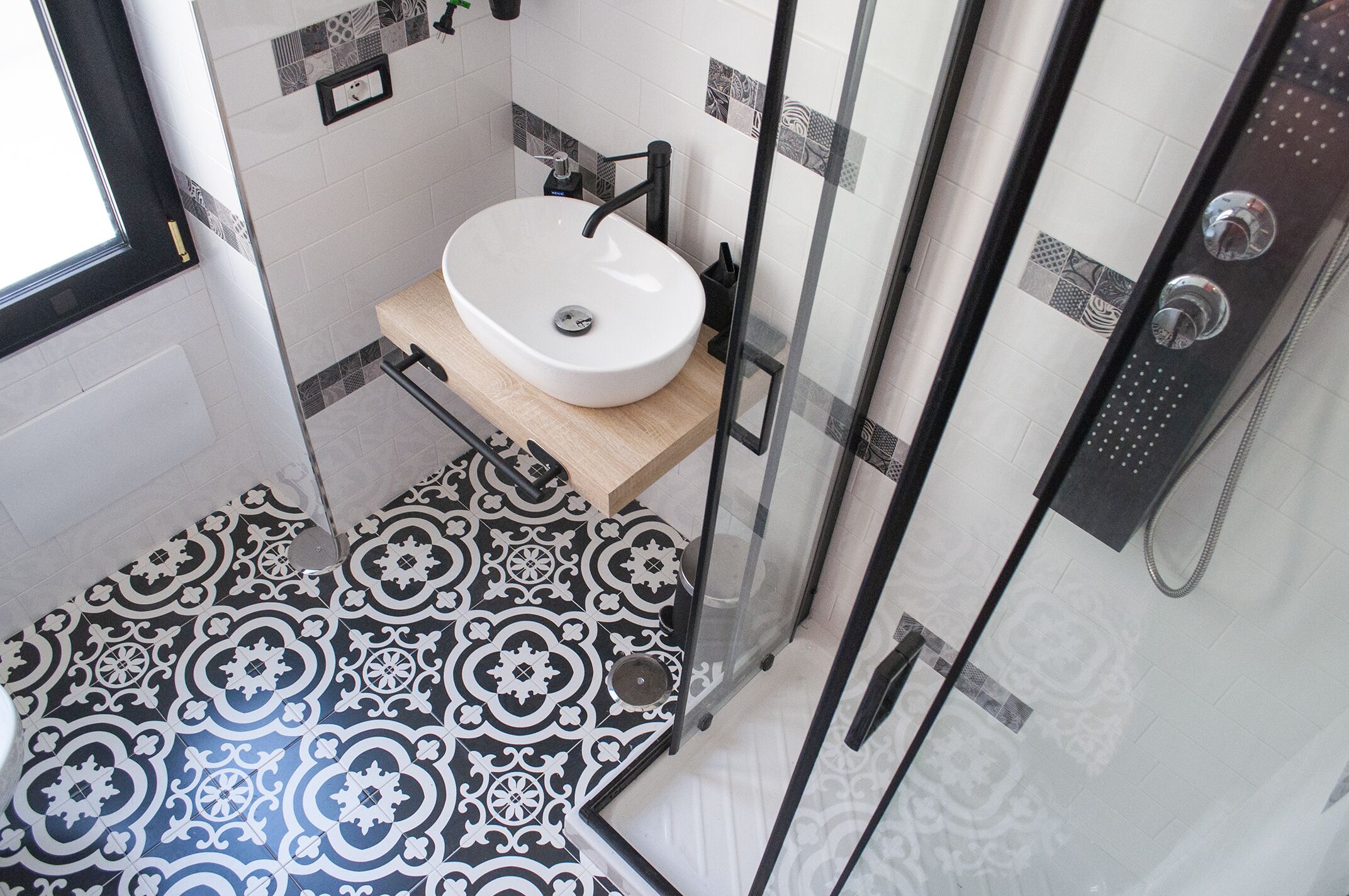 Une salle de bain avec un lavabo blanc, un carrelage noir et blanc et une douche à parois de verre.