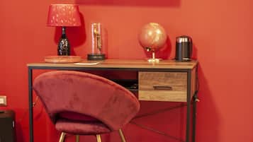 A room with a red wall, a flat-screen TV mounted above a wooden desk, a red velvet chair, a globe, and a coffee maker.